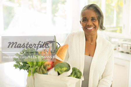 Portrait of smiling senior woman with groceries in kitchen
