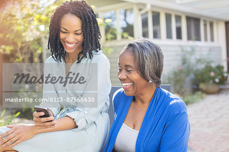 Smiling mother and daughter text messaging with cell phone on patio Smiling mother and daughter text messaging with cell phone on patio