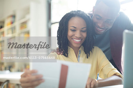 Happy couple reading paperwork at laptop Happy couple reading paperwork at laptop