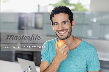 Portrait of smiling man eating apple in kitchen Portrait of smiling man eating apple in kitchen