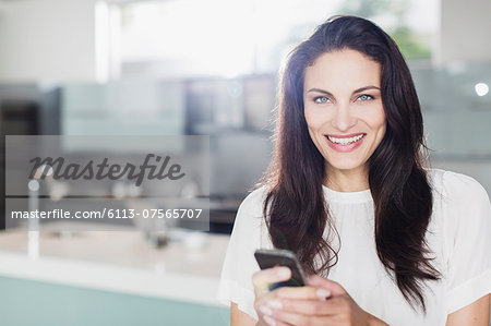 Portrait of smiling woman texting with cell phone in kitchen