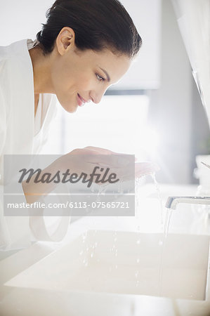 Woman in bathrobe splashing water on face