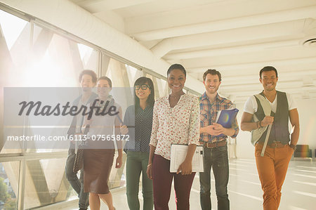 Confident creative business people walking in sunny corridor