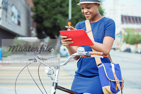 Casual businesswoman using digital tablet on bicycle on urban street