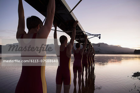 Rowing team carrying boat overhead into lake