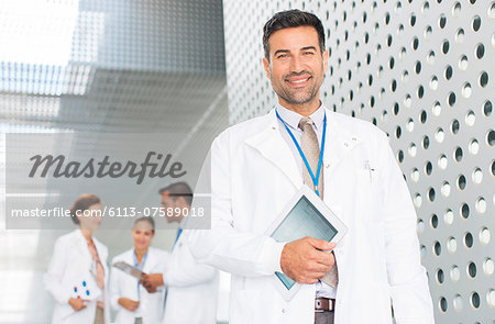 Portrait of confident doctor holding digital tablet in hospital corridor