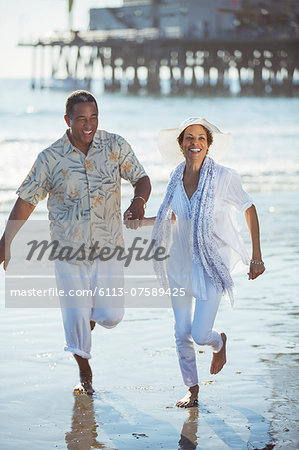 Smiling senior couple running on sunny beach