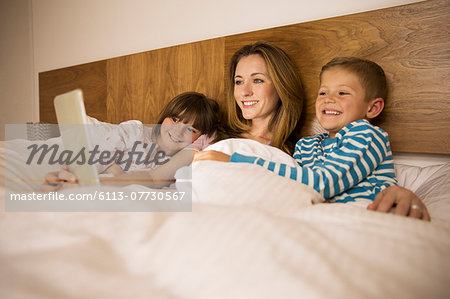 Mother and children using digital tablet in bed