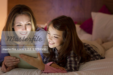 Mother and daughter using digital tablet on bed