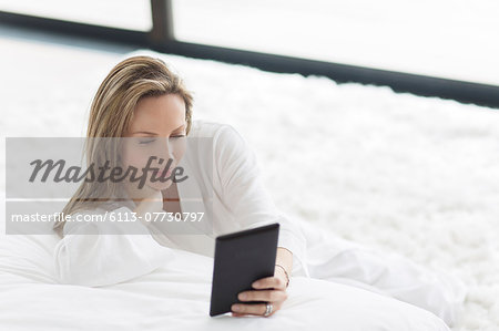 Woman in bathrobe using digital tablet in bedroom