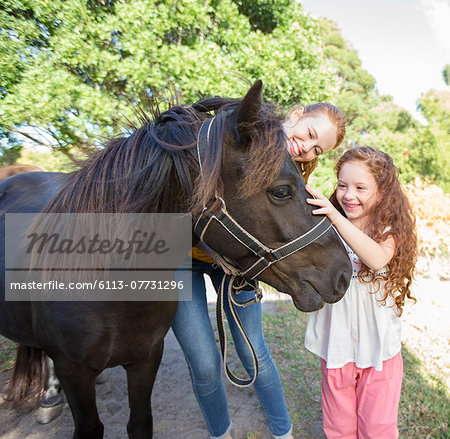 Mother and daughter petting horse outdoors