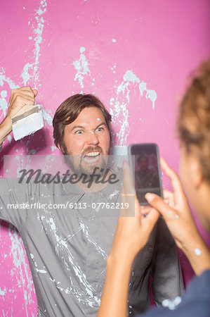 Woman taking picture with cell phone of man with paintbrush