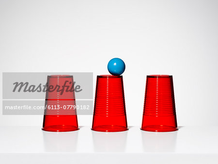 Blue ball balancing on middle of three red cups