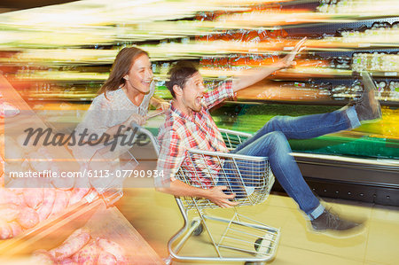 Blurred view of couple playing with shopping cart in grocery store