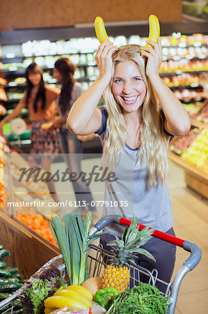 Woman playing with bananas while shopping in grocery store Woman playing with bananas while shopping in grocery store