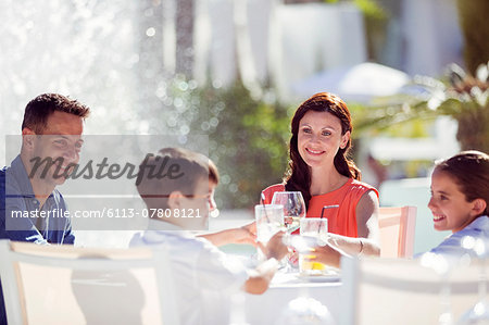 Family with two children raising toast at table outdoors