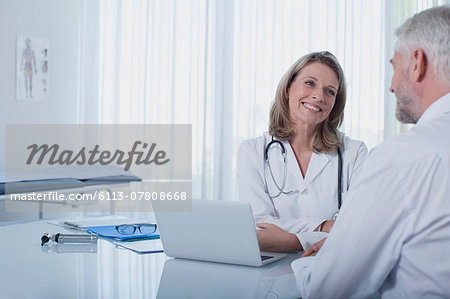 Smiling female doctor talking to patient at desk in office Smiling female doctor talking to patient at desk in office