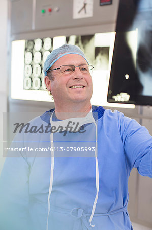 Smiling mature doctor wearing surgical clothing looking at x-ray in hospital