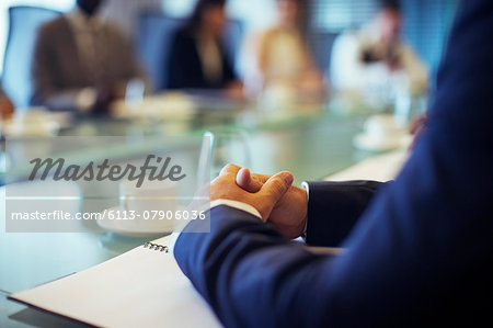 Businessman sitting at conference table in conference room with hands clasped