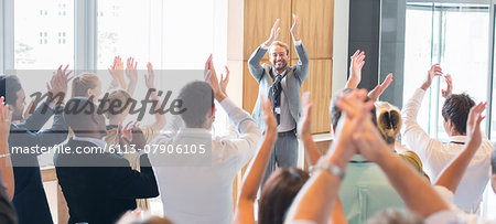 Portrait of smiling man standing before audience in conference room, applauding