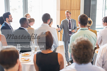 Portrait of smiling man standing in conference room, offering microphone to person in audience