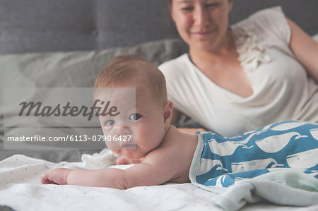 Portrait of little baby lying on bed with mother smiling in background