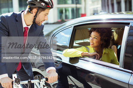 Businessman on bicycle talking to woman in car