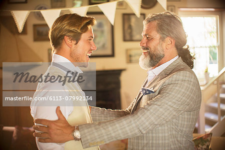 Best man and bridegroom standing and laughing in domestic room