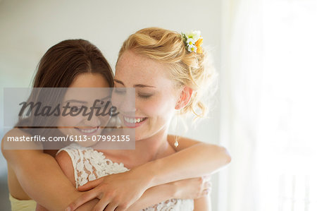 Bridesmaid embracing bride in bedroom