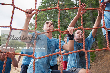 Determined woman climbing net at boot camp obstacle course