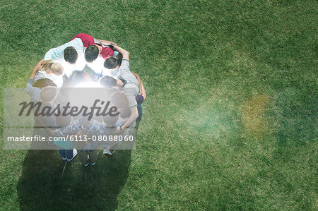 Team huddled in circle around glowing orb in field Team huddled in circle around glowing orb in field