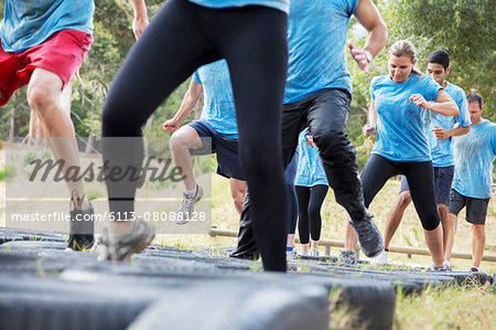 Determined people jumping tires on boot camp obstacle course