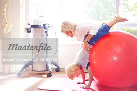 Physical therapist holding boy over large fitness ball