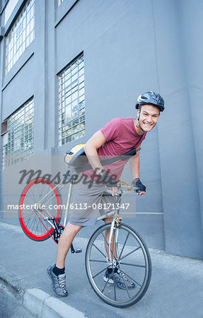 Portrait smiling bicycle messenger with helmet leaning forward on urban sidewalk