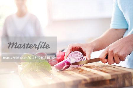 Woman slicing red onion on cutting board in kitchen