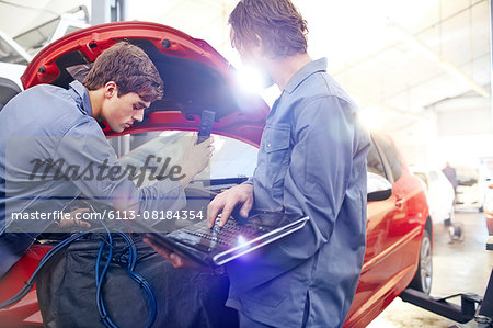 Mechanics with laptop working on car engine in auto repair shop