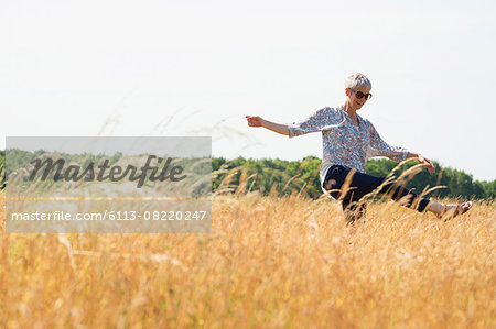 Playful senior woman dancing in sunny rural field Playful senior woman dancing in sunny rural field