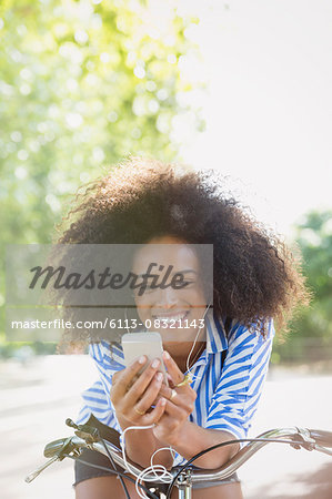 Smiling woman with afro listening to music with headphones and mp3 player on bicycle