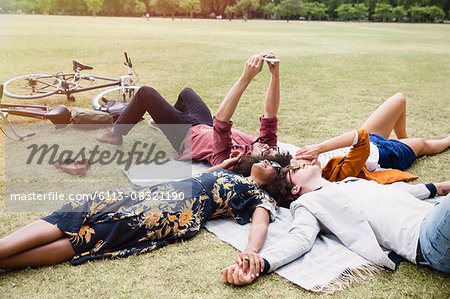 Friends relaxing and taking selfie in circle on blanket in park
