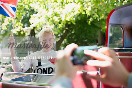 Woman waving British flag being photographed on double-decker bus