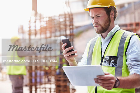 Construction worker with digital tablet texting with cell phone at construction site