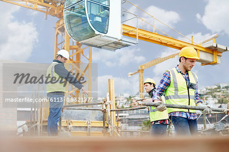 Foreman guiding construction workers below crane at construction site