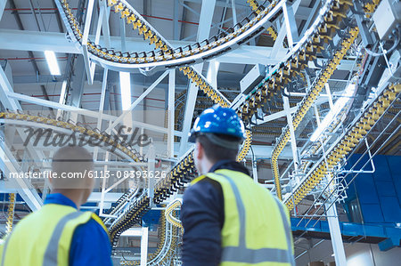 Workers looking up at winding printing press conveyor belts overhead Workers looking up at winding printing press conveyor belts overhead
