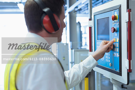 Worker with ear protectors at control panel in machinery