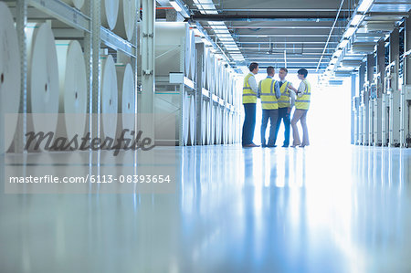 Workers talking near large paper spools in printing plant