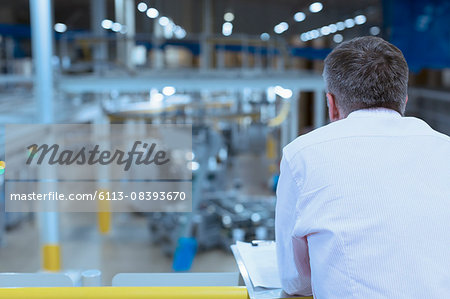 Supervisor with clipboard on platform overlooking factory