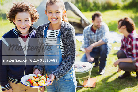Portrait smiling brother and sister with vegetable skewers at campsite