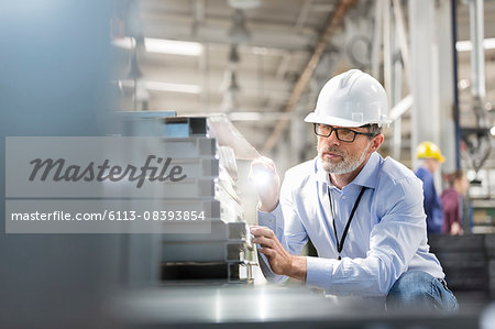 Engineer examining steel parts with flashlight in factory