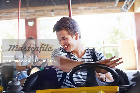 Smiling young man riding bumper cars at amusement park