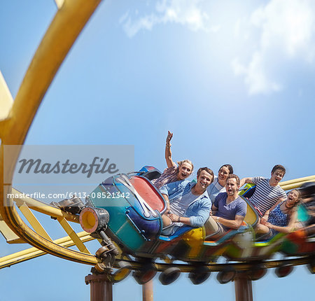 Cheering friends riding roller coaster at amusement park Cheering friends riding roller coaster at amusement park